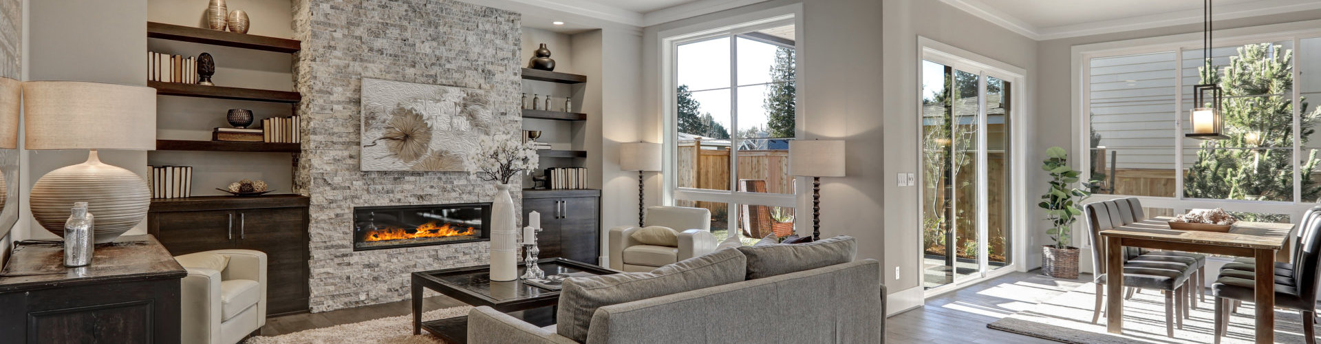 living room interior in gray and brown colors features gray sofa atop dark hardwood floors facing stone fireplace with built-in shelves