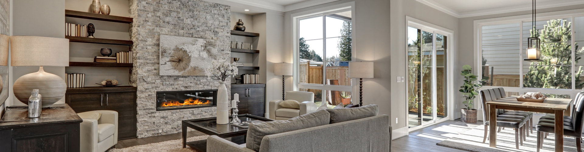 living room interior in gray and brown colors features gray sofa atop dark hardwood floors facing stone fireplace with built-in shelves